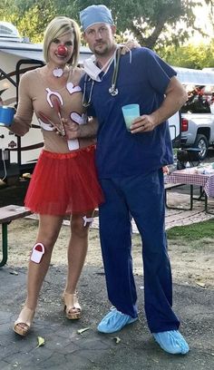 a man and woman in costumes standing next to each other at a picnic table with food on it