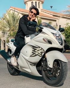 a man sitting on top of a white motorcycle in front of a building with palm trees