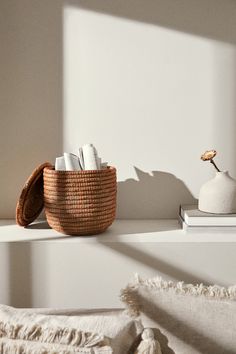 a wicker basket sitting on top of a white shelf next to a vase and books