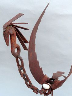 a rusted metal bird sculpture with chains on it's neck and two eggs in its beak