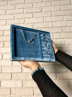 a person holding up a blue box with jewelry in it on top of a brick wall