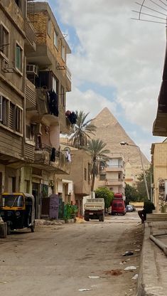 an empty street with cars parked in front of buildings and the pyramids behind it