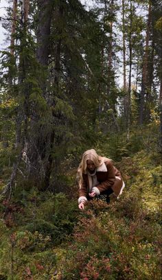 a woman crouches down in the woods