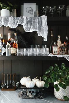 an assortment of liquor bottles and glasses on a shelf with white pumpkins in the foreground