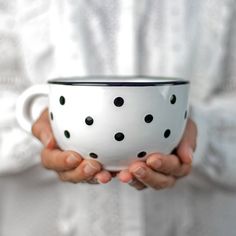 a woman holding a white and black polka dot coffee cup