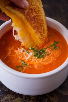 a person dipping cheese into a bowl of tomato soup with parmesan bread on top