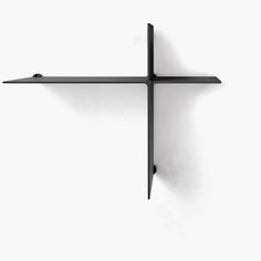 a cross made out of black metal on a white wall with no one around it