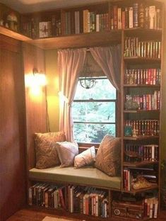 a window seat in front of a bookshelf filled with lots of books and pillows