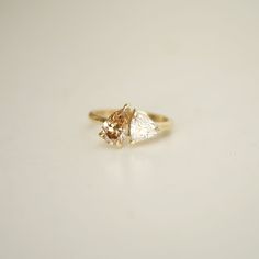 a gold ring with two pear shaped diamonds on the front and center, sitting on a white surface