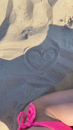 a woman laying on top of a sandy beach next to a pink flip - flop