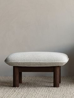 a white ottoman sitting on top of a carpeted floor next to a gray wall