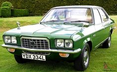 a green car parked on top of a lush green grass covered field next to a hedge