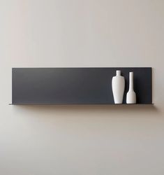 two white vases sitting on top of a black shelf next to a gray wall