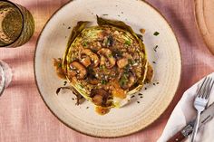 a white plate topped with artichoke covered in mushrooms and sauce next to a glass of wine