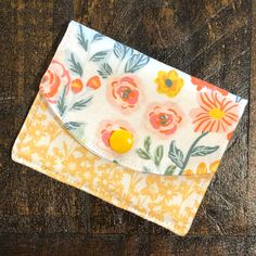 an orange and white flowered wallet sitting on top of a wooden table next to a yellow button