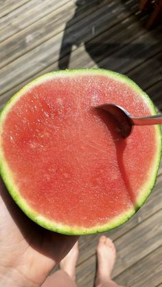 a piece of watermelon is being held by a person's hand with a spoon