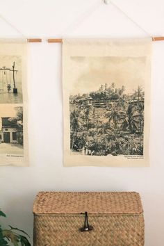 two pictures are hanging on the wall above a wicker box and plant in front of it