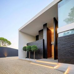 an entrance to a modern house with trees in the front yard and brick walkway leading up to it