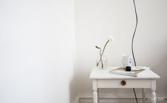 a white table with a book, coffee cup and vase on it