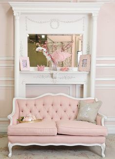 a pink couch sitting in front of a white fireplace next to a mirror and table