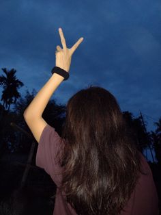 a woman is holding her hand up in the air at night with palm trees behind her