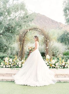 a bride standing in front of an arch with flowers and greenery