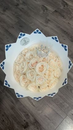 a bouquet of white roses with a tiara on top in a paper box, sitting on a wooden floor