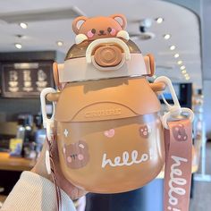 a person holding up a brown teddy bear shaped cup with the word hello on it