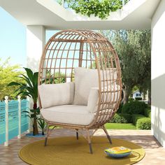 a wicker hanging egg chair with cushions on a rug in front of a pool