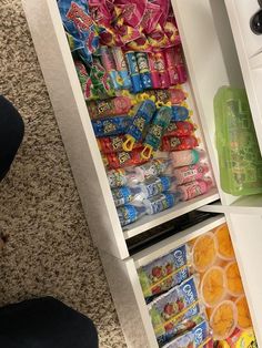 a person standing in front of an open refrigerator filled with snacks and candy bar wrappers