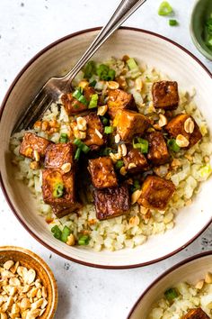 two bowls filled with rice and tofu on top of a white table next to other dishes