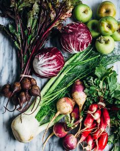 many different types of vegetables are laid out on the counter top, including onions, radishes and apples