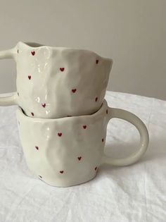 two coffee mugs with hearts on them sitting on a white tableclothed surface