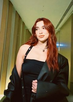 a woman with long red hair wearing a black dress and jacket posing for the camera