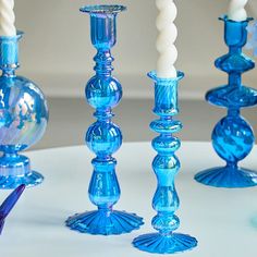 several blue glass candlesticks are lined up on a white table with one candle in the middle