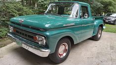 an old green truck is parked on the side of the road in front of some trees