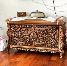 an ornately carved wooden chest on the floor in a room with wood floors and white walls