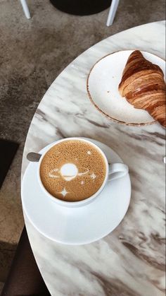 a cup of coffee and croissant on a marble table