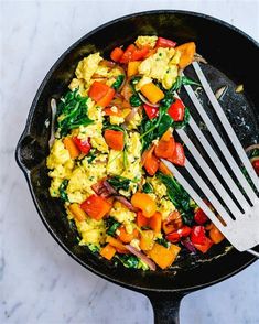 a skillet filled with eggs and vegetables on top of a white counter next to a fork