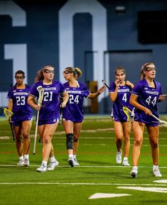 the girls lacrosse team is walking on the field with their sticks in hand and wearing purple uniforms