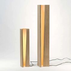 two tall wooden lamps sitting next to each other on a white surface with wires running through them