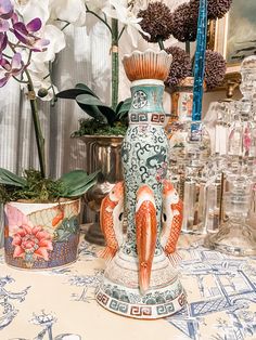 there are vases with fish on them and flowers in pots behind them, along with other glassware