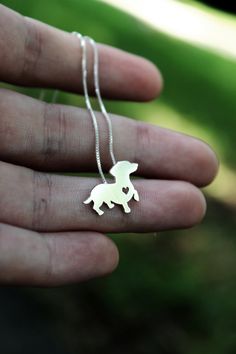 a person is holding a small silver dog necklace