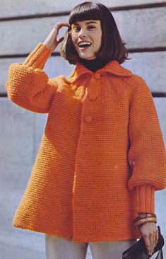 a woman in an orange coat talking on her cell phone while holding a handbag