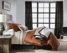 a bed with two pillows and blankets on it in front of a large window next to a chair