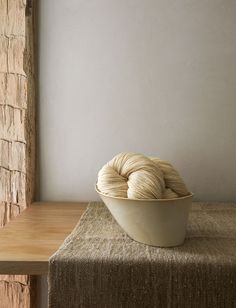 two balls of yarn sit in a bowl on a table next to a brick wall