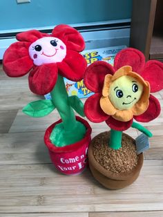 two stuffed flowers sitting on top of a wooden floor next to a potted plant