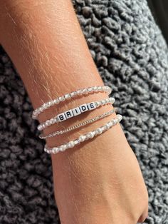 a woman wearing three bracelets with the word bride written on one side and two white beads