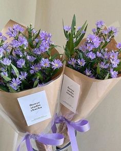 two bouquets of purple flowers wrapped in brown paper and tied with a purple ribbon