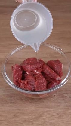 someone pours water into a bowl filled with raw meat on a wooden table top